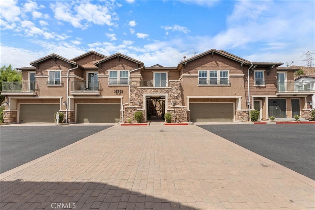 Multi-unit residential building with tan stucco, stone accents, balconies, and garages along a paved driveway.