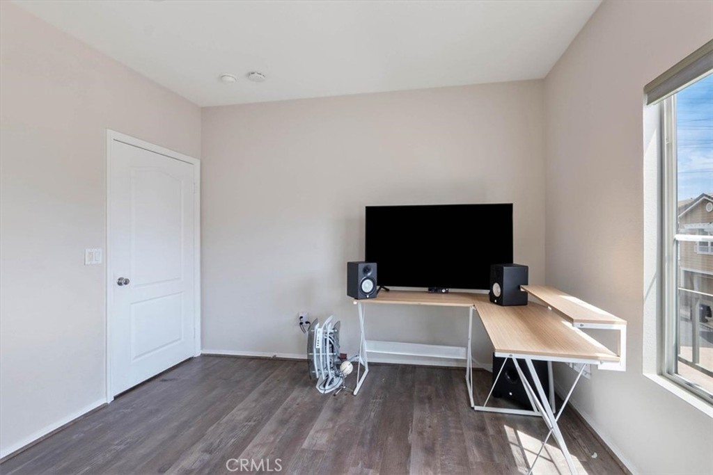 Home office with gray plank flooring, a long wood desk, television, and large window.