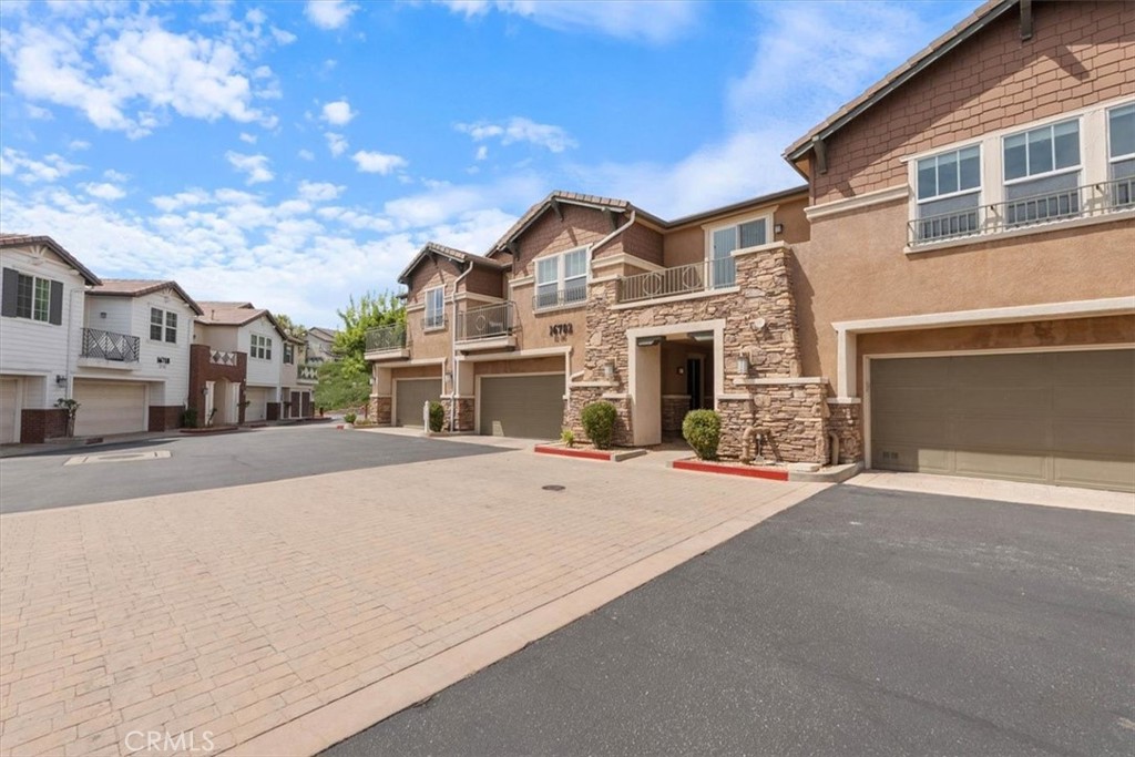 Attached tan townhomes with stone accents and balconies facing a paved shared driveway.