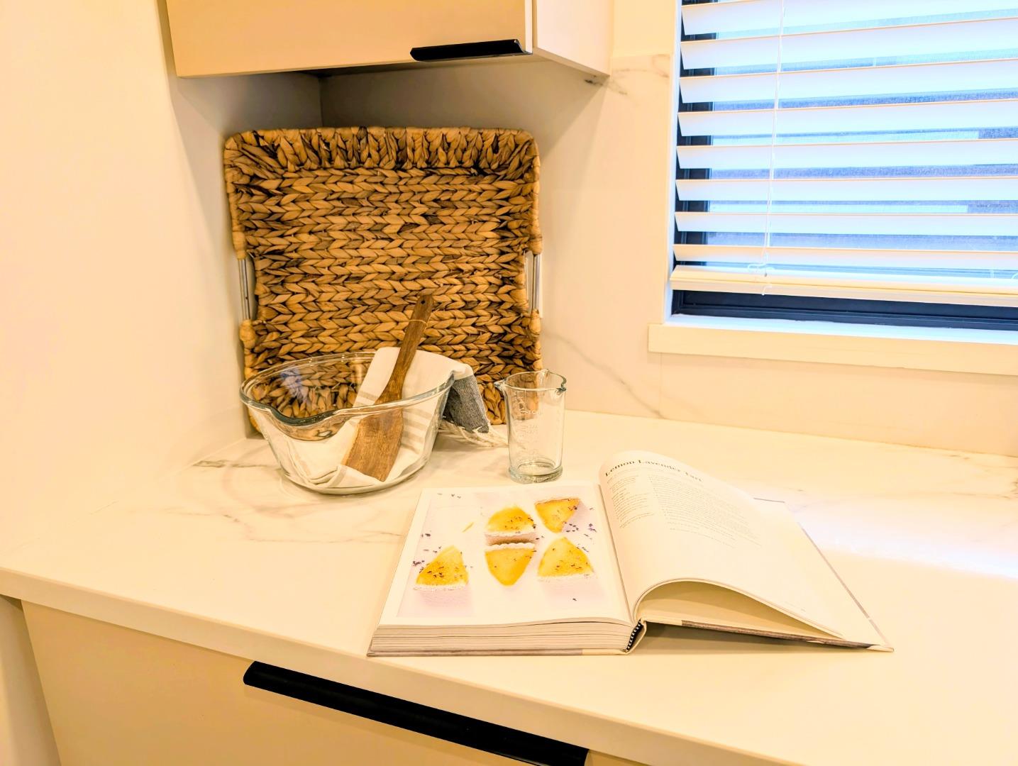 Kitchen counter with an open cookbook, glass containers, and a woven basket beneath a window.