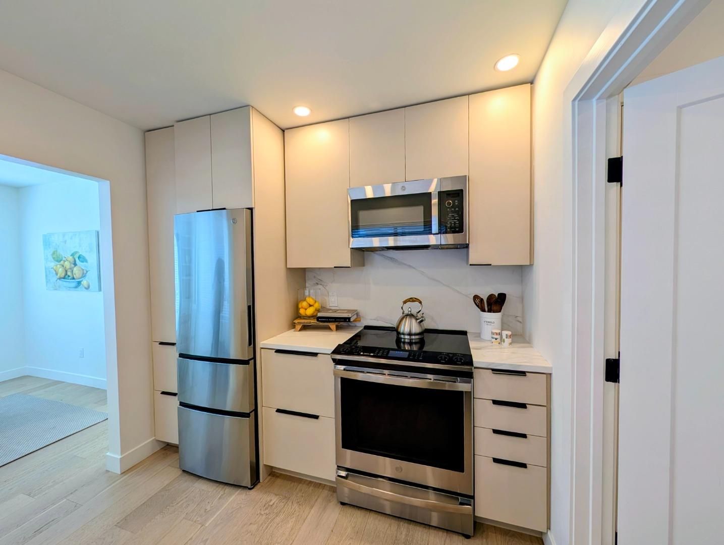 Modern kitchen with white cabinets, stainless steel appliances, and light wood floors.