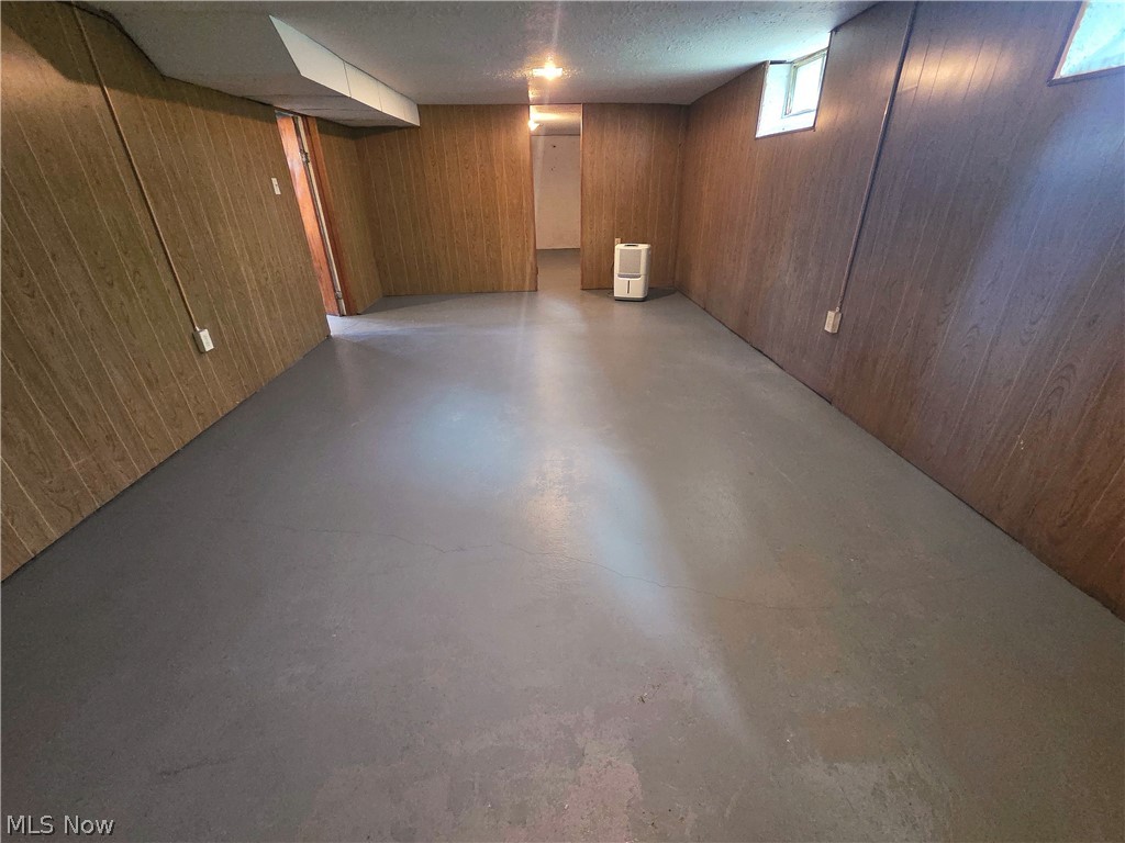 Vacant basement room with brown paneled walls, concrete floor, high windows, and a portable heater.