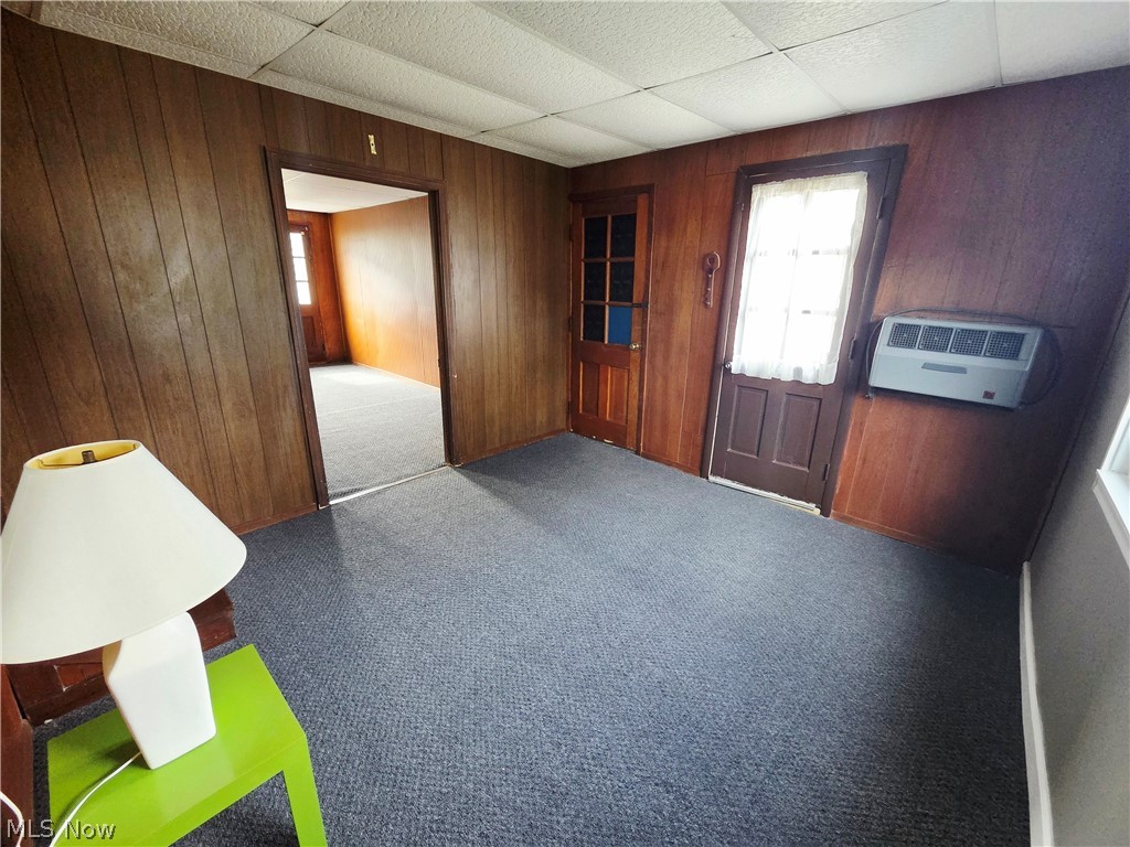 Wood-paneled room with gray carpet, glass-paneled door, and window air conditioner.