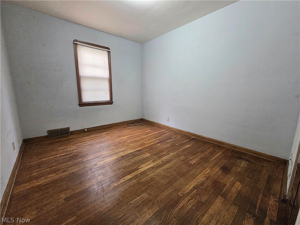 Empty room with hardwood floors, pale walls, and a window with blinds.