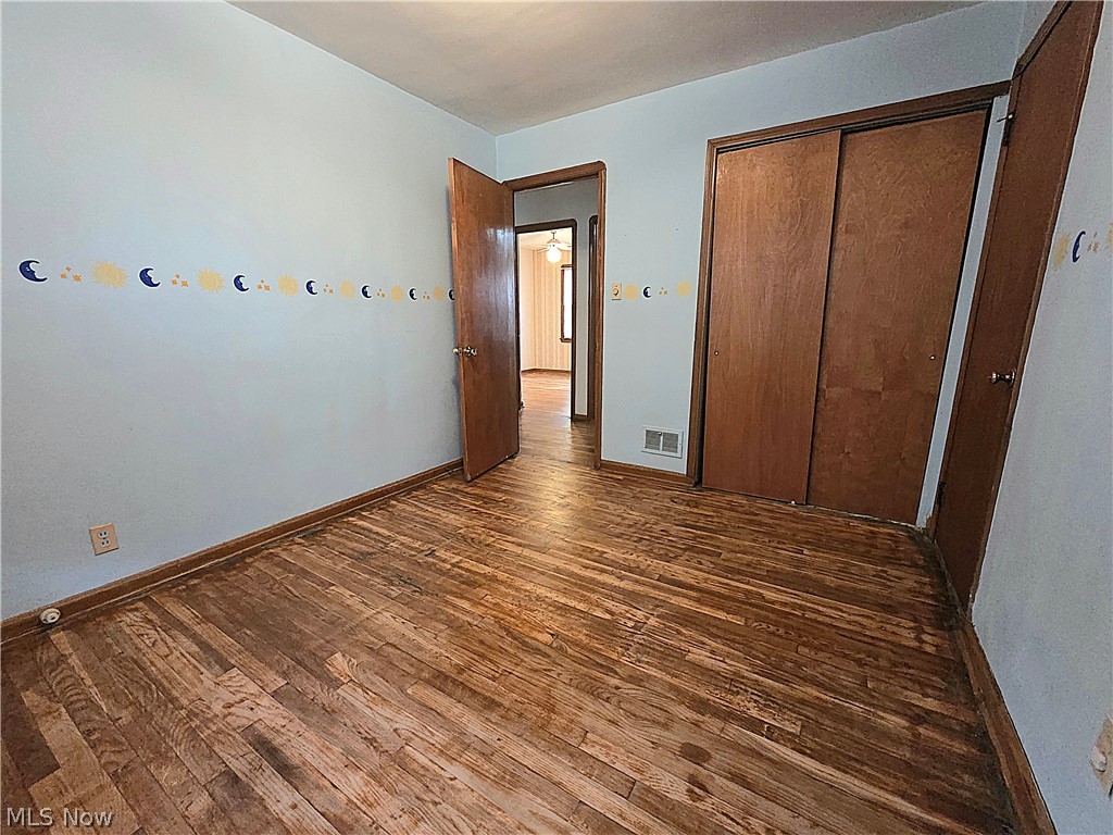 Empty bedroom with worn hardwood floors, a moon-and-star wall border, and wooden sliding closet doors.