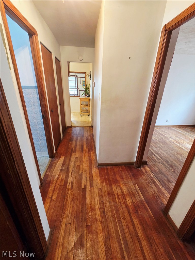 Hallway with polished hardwood floors, dark wood trim, and open doorways to adjoining rooms.