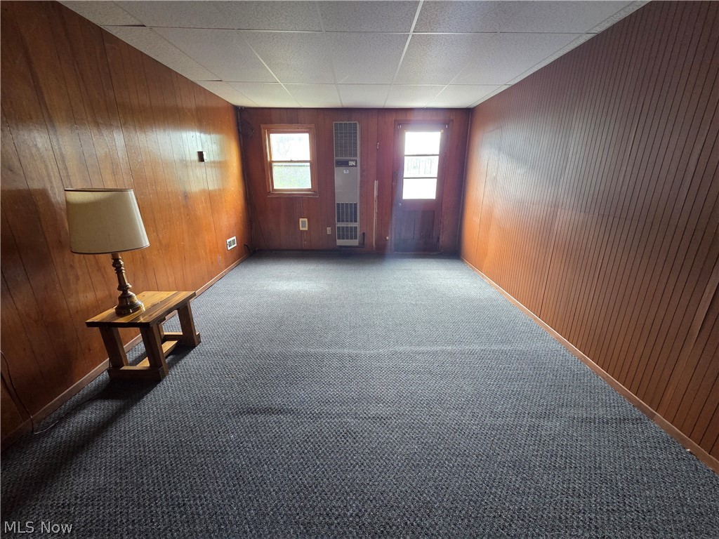 Mostly empty carpeted room with wood-paneled walls, two windows, and a small table with a lamp.