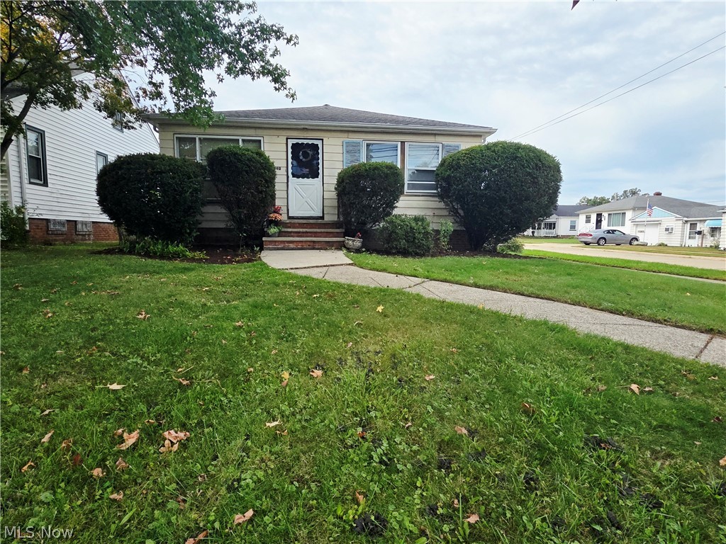 Single-story home with light siding, trimmed shrubs, and a walkway through the front lawn.
