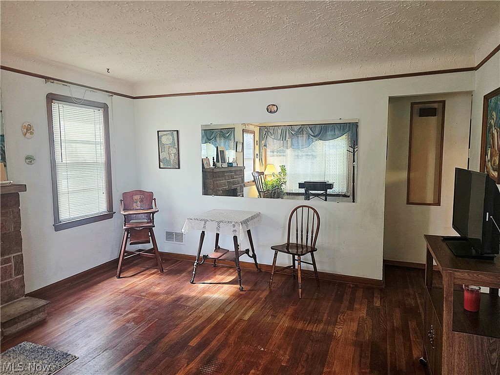 Living and dining room with dark hardwood floors, brick fireplace, and a wide opening to the adjoining room.