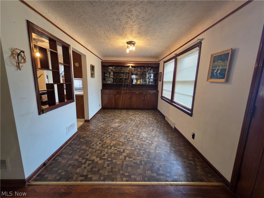 Empty dining room with parquet flooring, a built-in china cabinet, and kitchen pass-through.