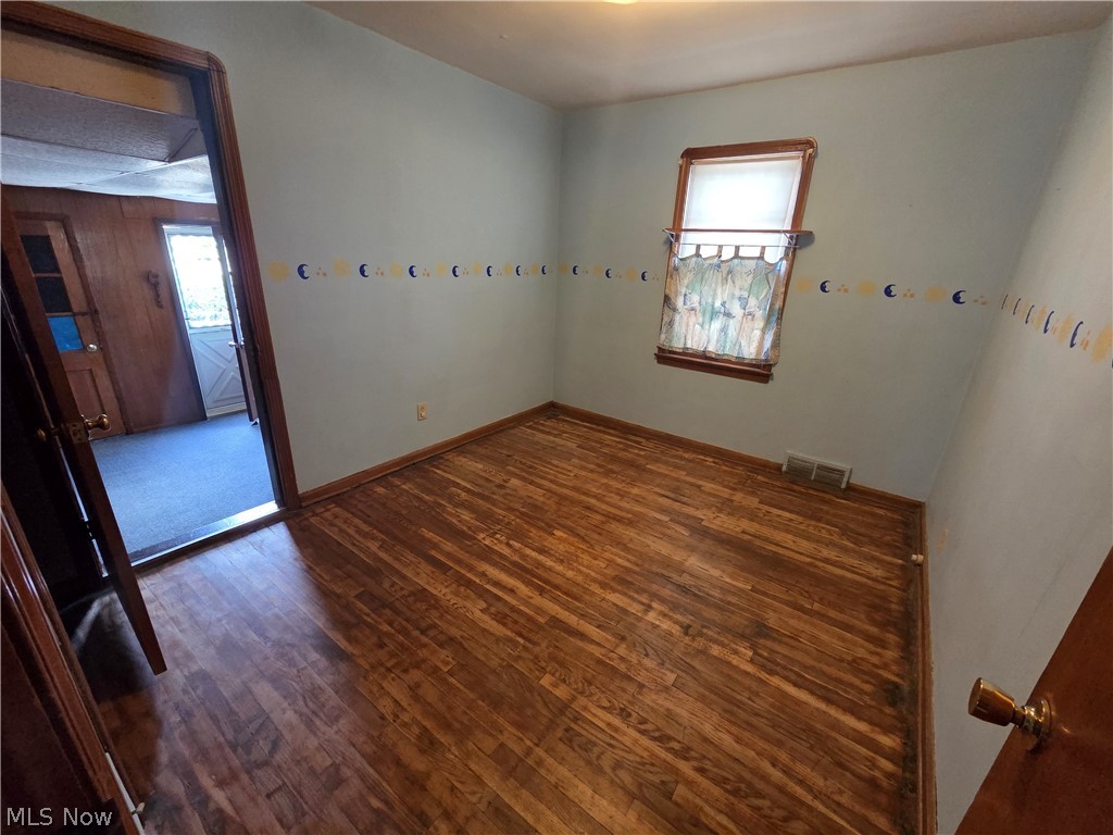 Empty room with hardwood floors, a curtained window, and a decorative wall border.