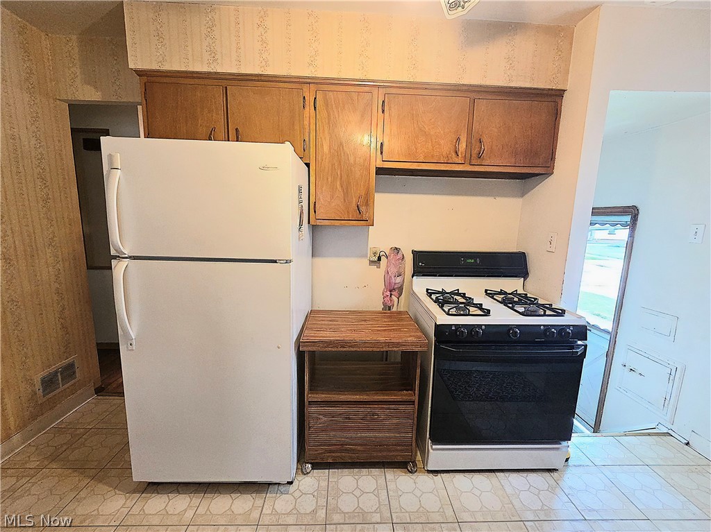 Compact kitchen with wood cabinets, a white refrigerator, and a black gas range.