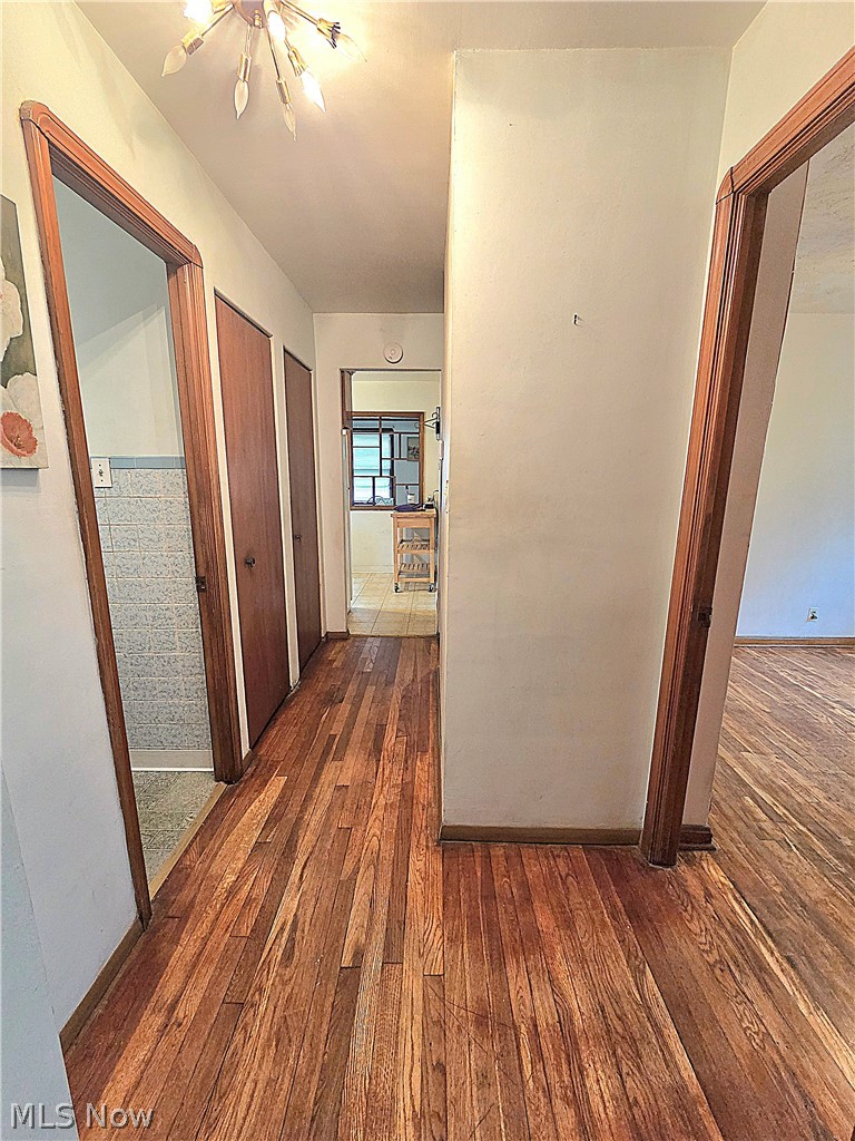 Hallway with hardwood floors, wood-trimmed doorways, and a chandelier.