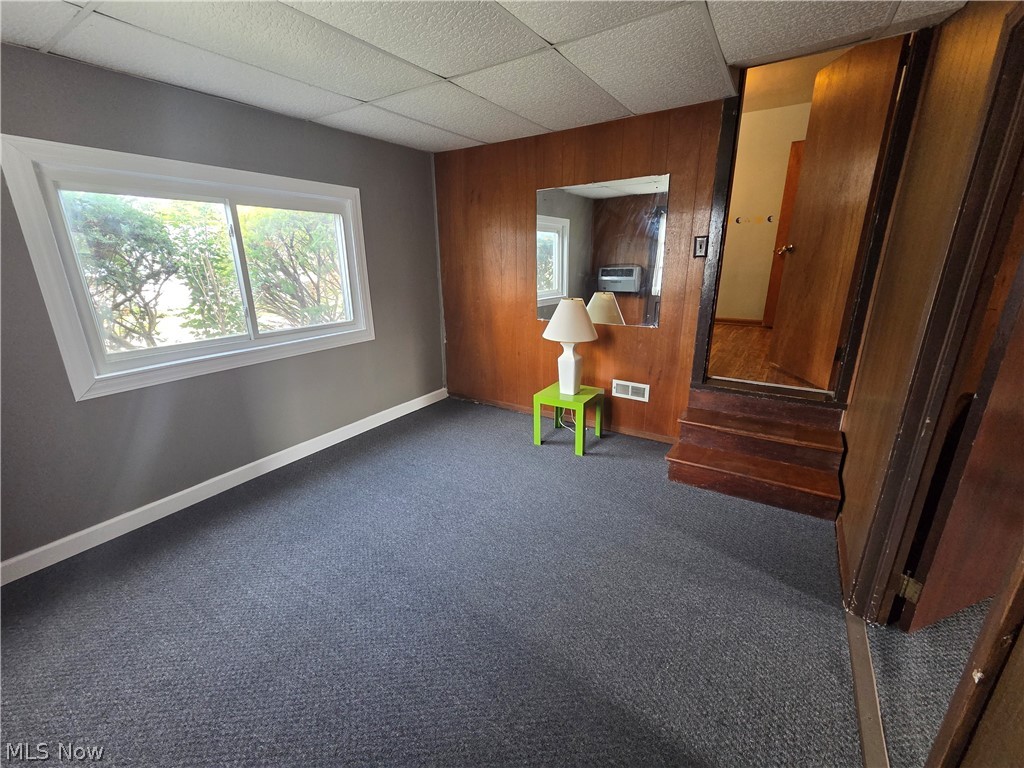 Carpeted room with a large window, wood-paneled wall, mirror, and steps to a doorway.