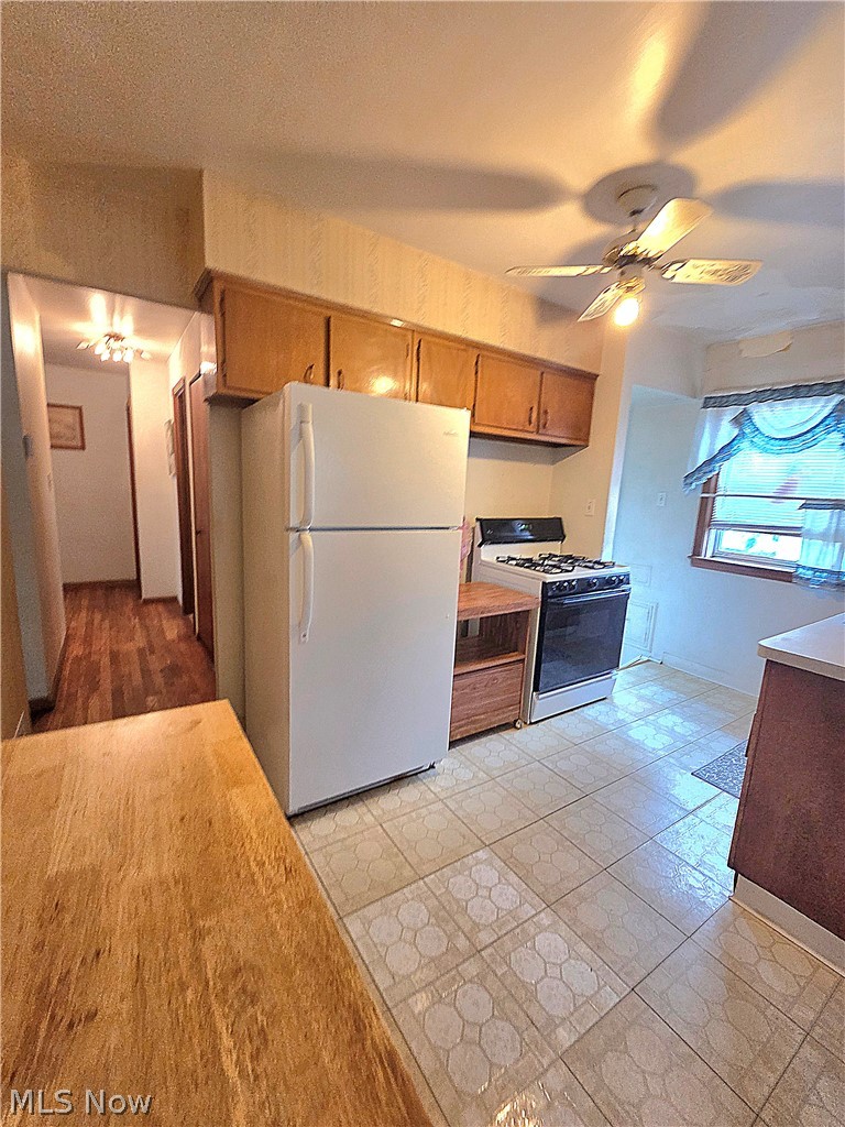 Kitchen with wood cabinets, white refrigerator, gas range, and patterned tile floor.