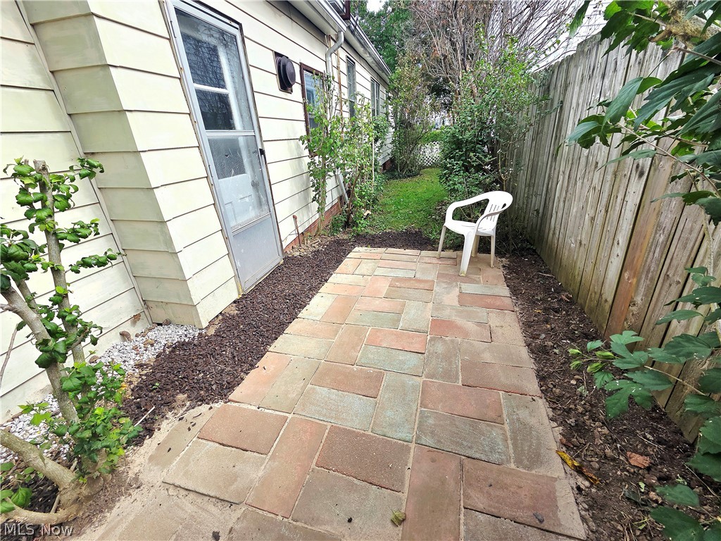 Side-yard patio with multicolored pavers, a white chair, and a tall wooden fence.