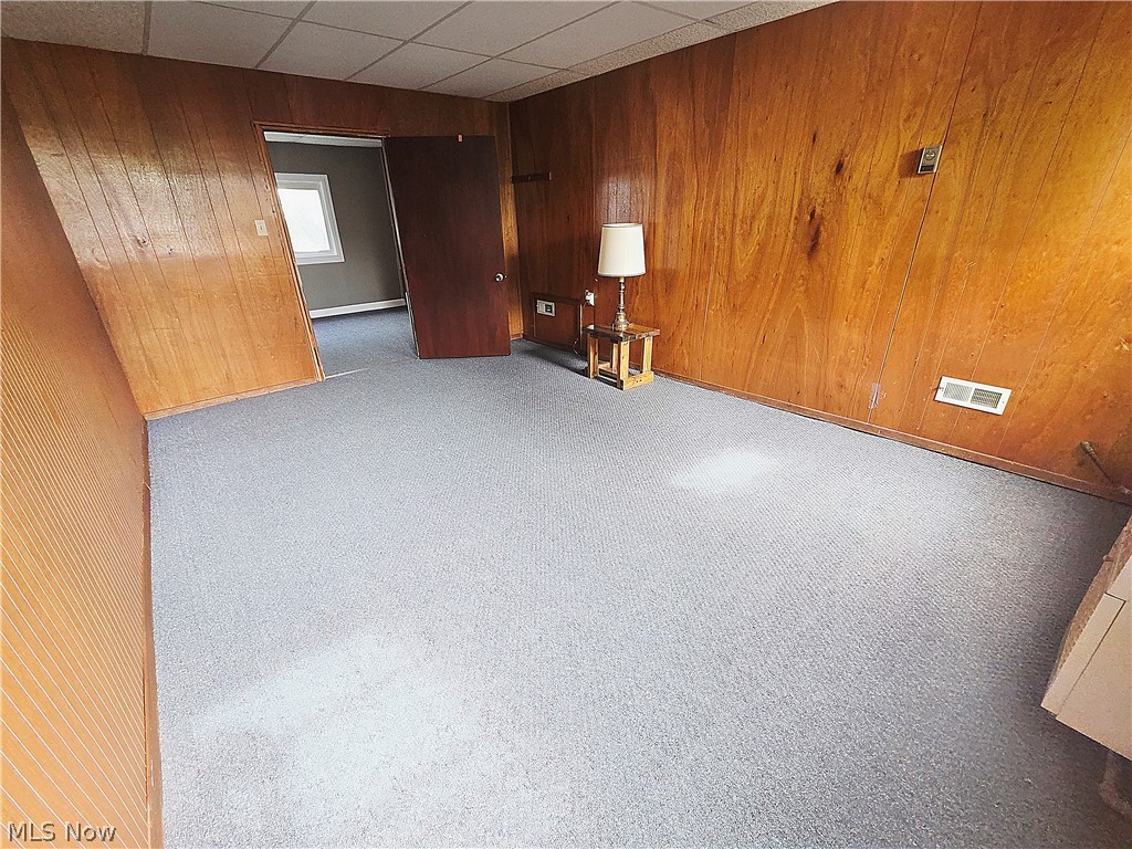 Carpeted room with wood-paneled walls, a drop ceiling, and an open doorway.