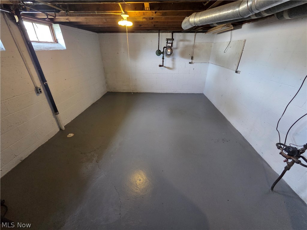 Empty basement with a concrete floor, white block walls, exposed joists, and utility piping.