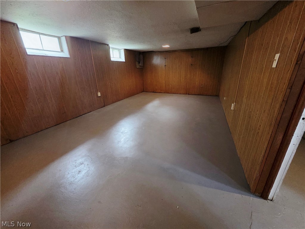 Empty basement room with wood-paneled walls, a bare concrete floor, and two small high-set windows.