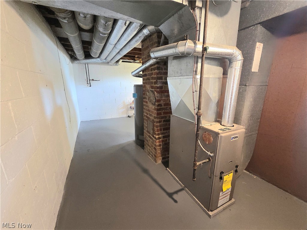 Unfinished basement utility area with a furnace, exposed ductwork, and brick chimney.