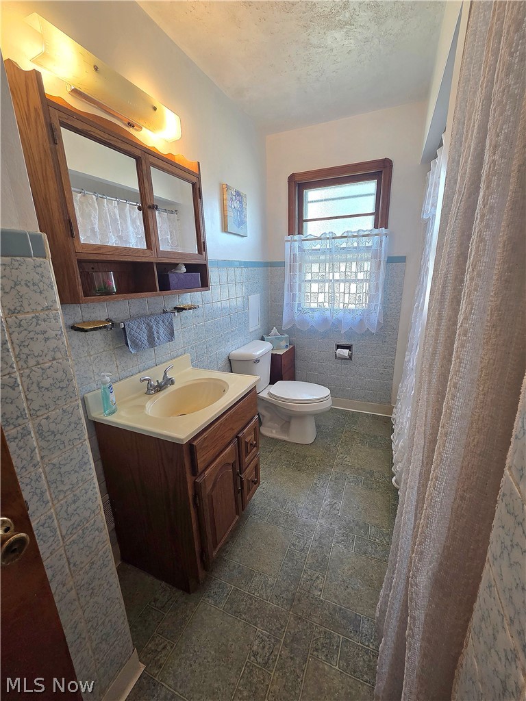 Bathroom with a wood vanity, blue-gray tile, and lace curtains on the window.