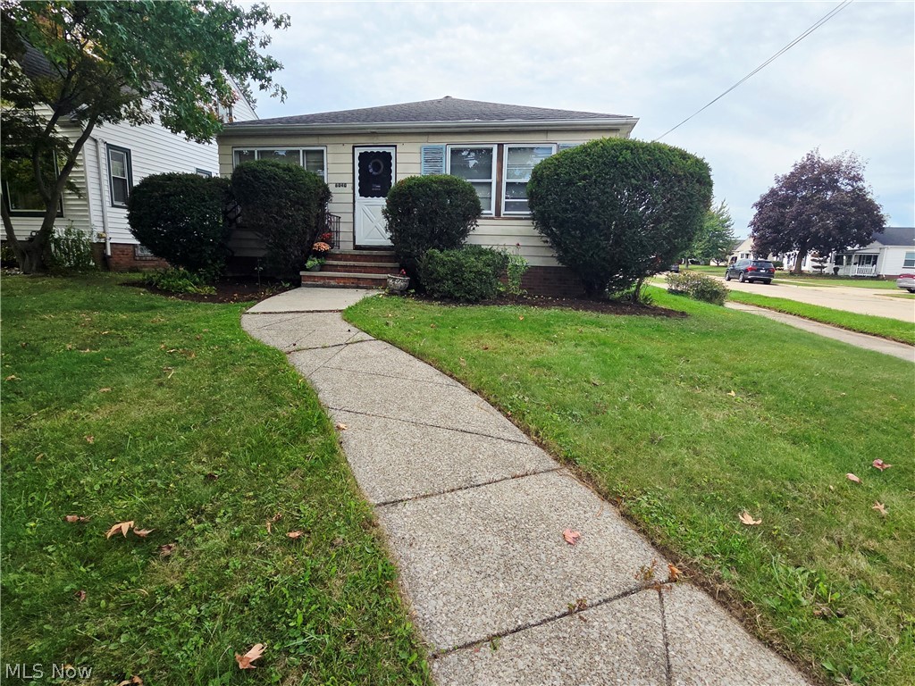Single-story home's front exterior with a curved concrete walkway and trimmed shrubs.
