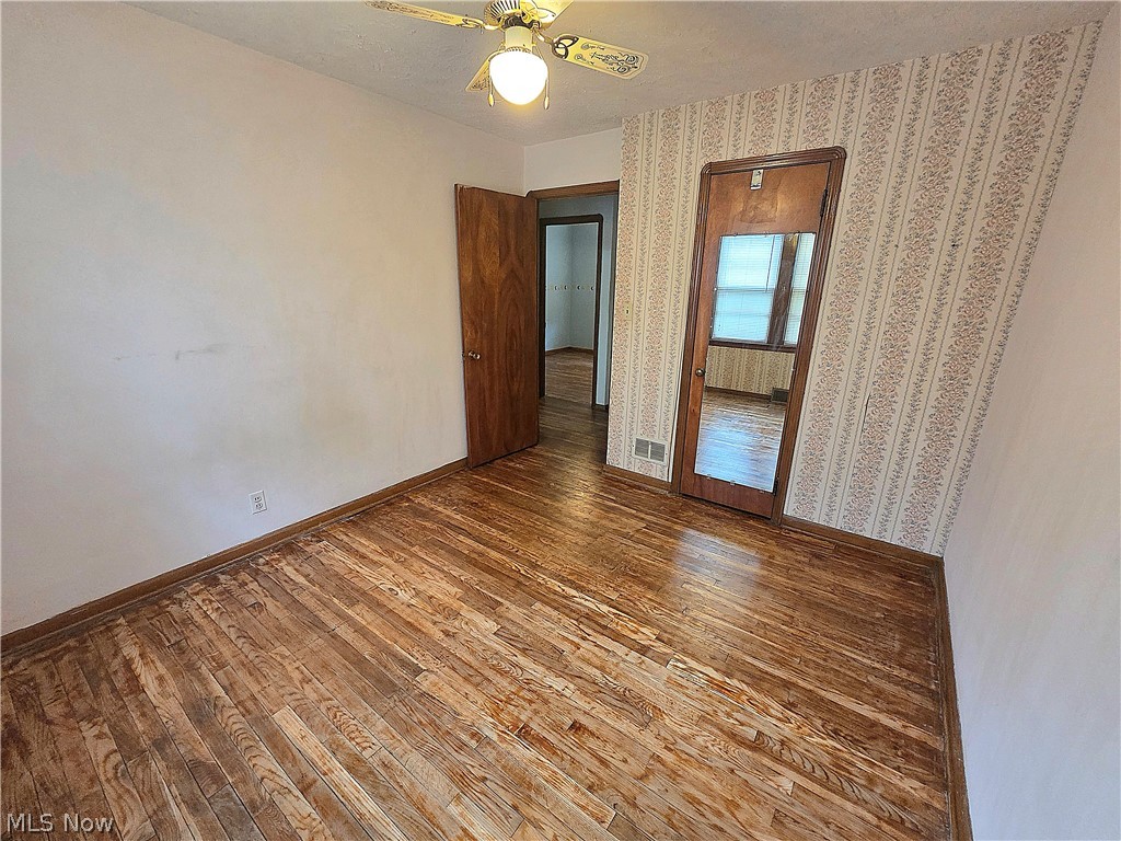 Vacant room with worn hardwood floors, patterned wallpaper, and a mirrored closet door.