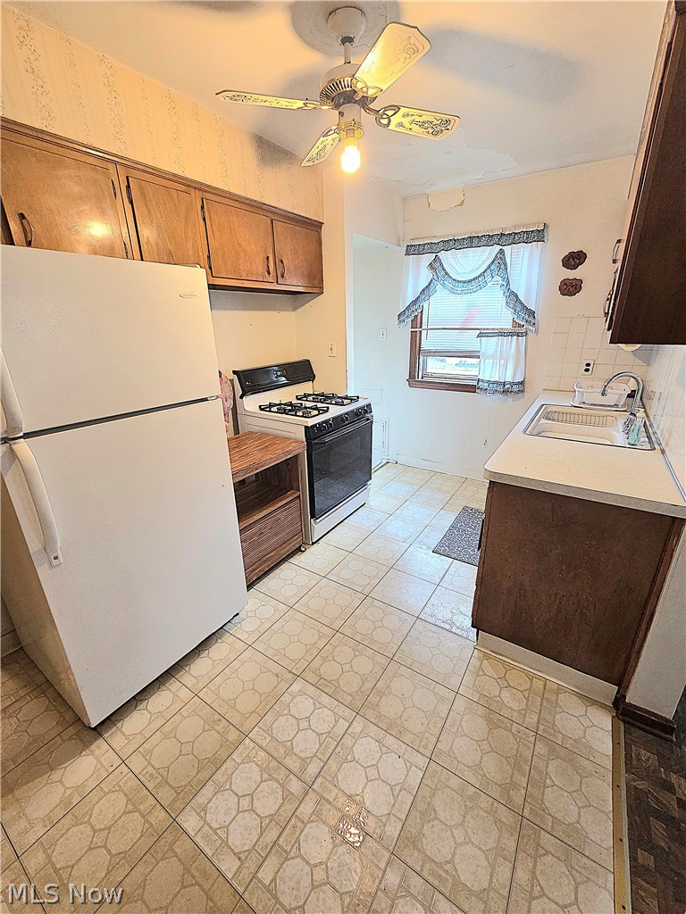 Kitchen with dark wood cabinets, a white refrigerator, gas range, and patterned tile floor.