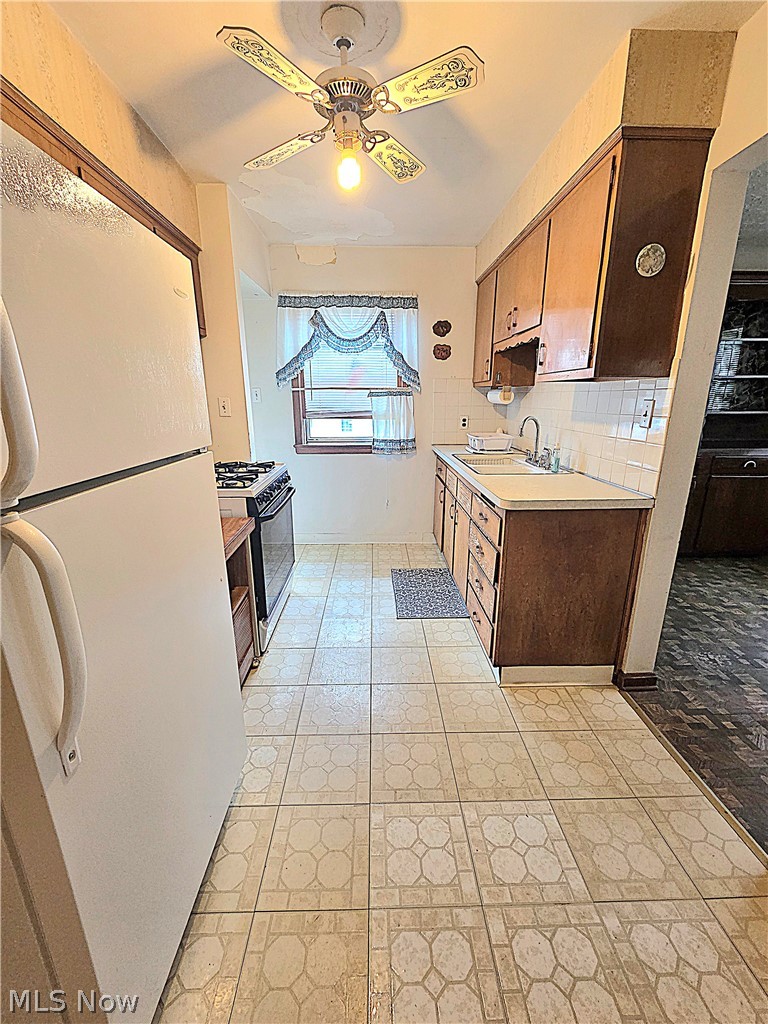 Galley kitchen with brown cabinets, white refrigerator, gas stove, and patterned tile floor.