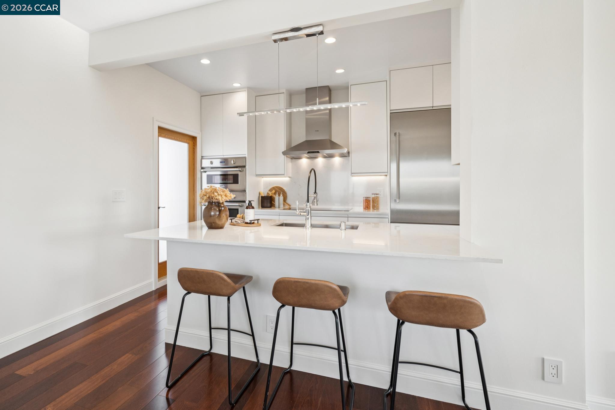Modern kitchen with a white island, stainless steel appliances, and three brown bar stools.