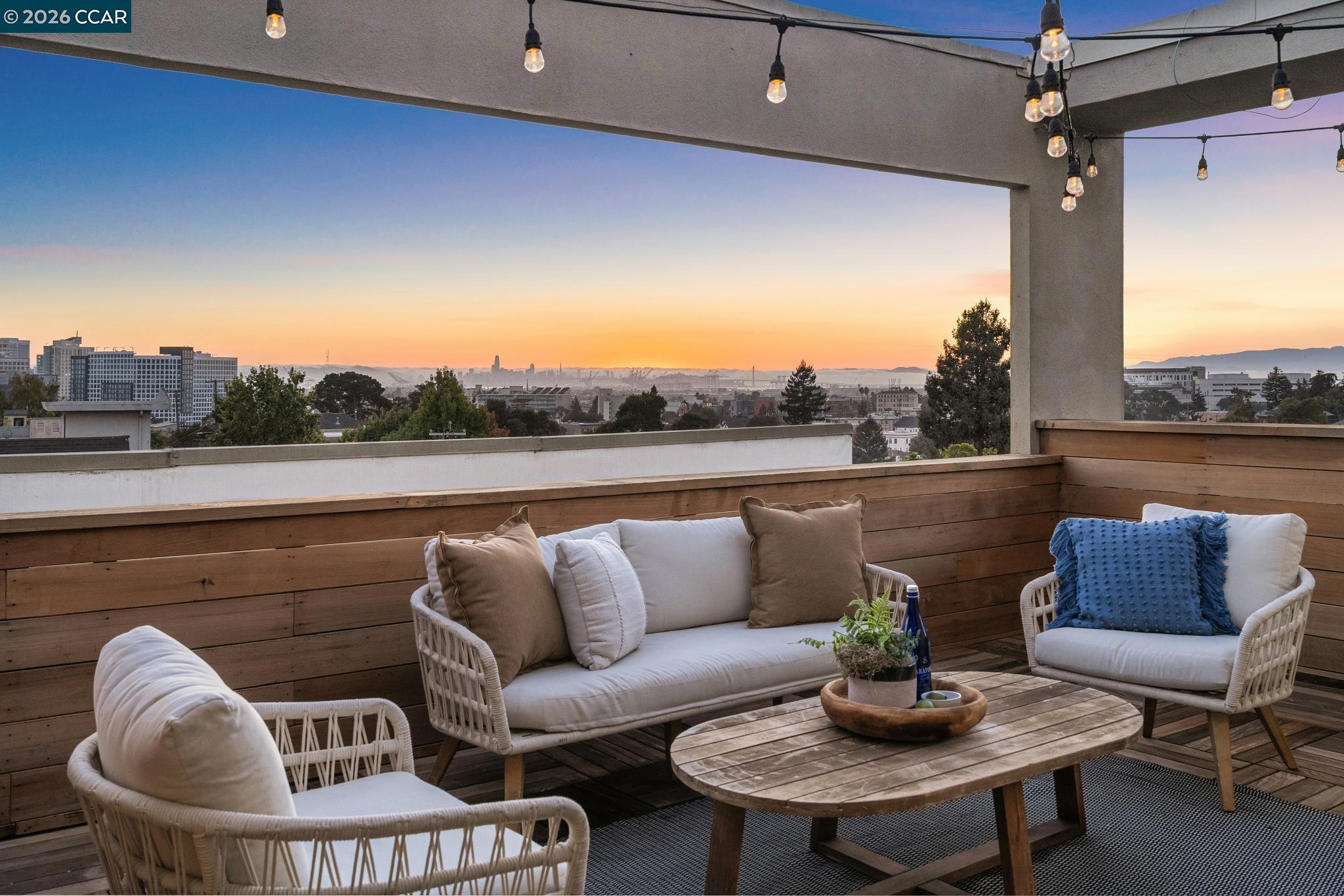 Rooftop deck with wicker seating and a city skyline view at sunset.