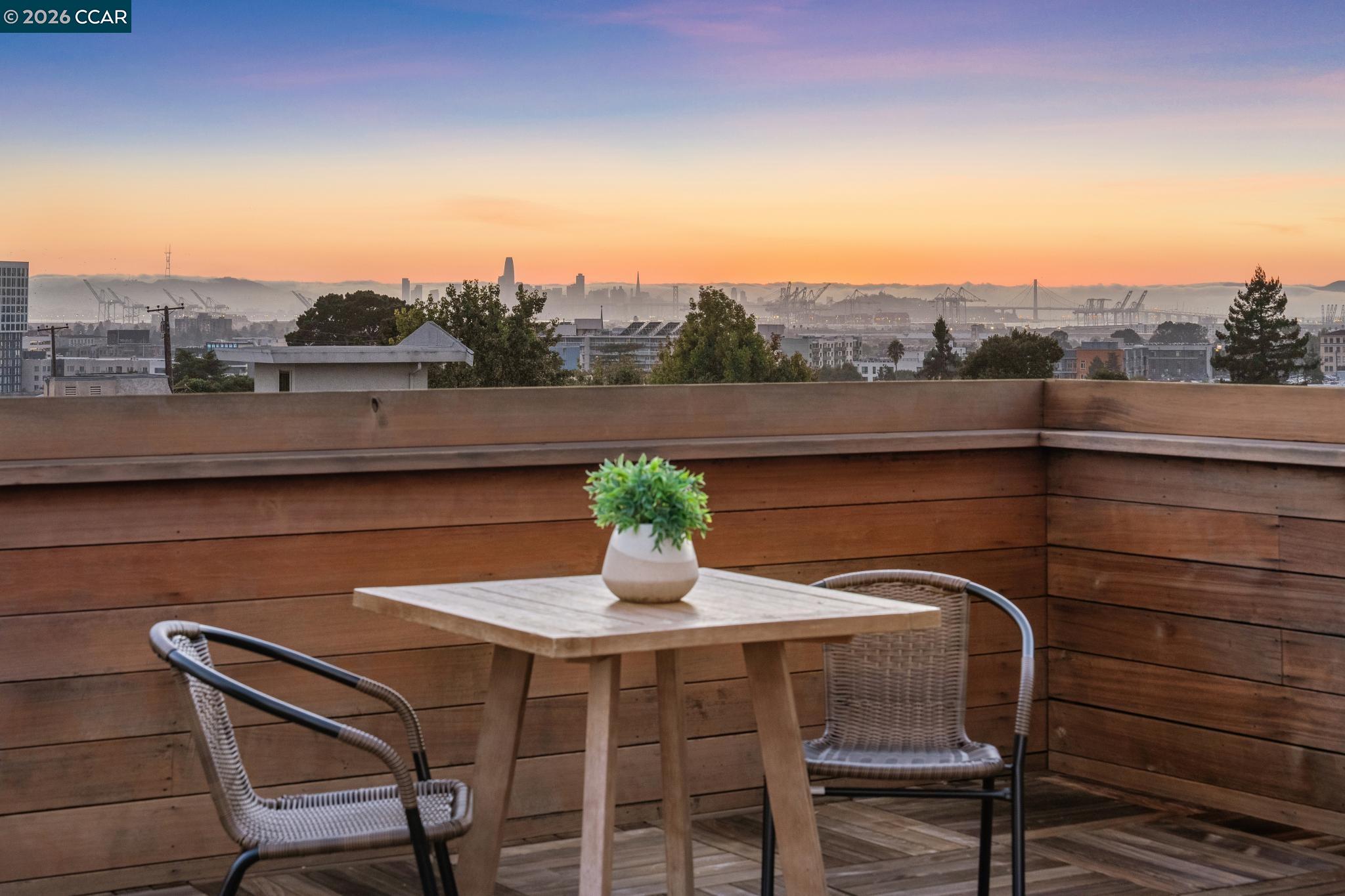 Rooftop terrace with woven chairs and a table overlooking the city skyline at sunset.