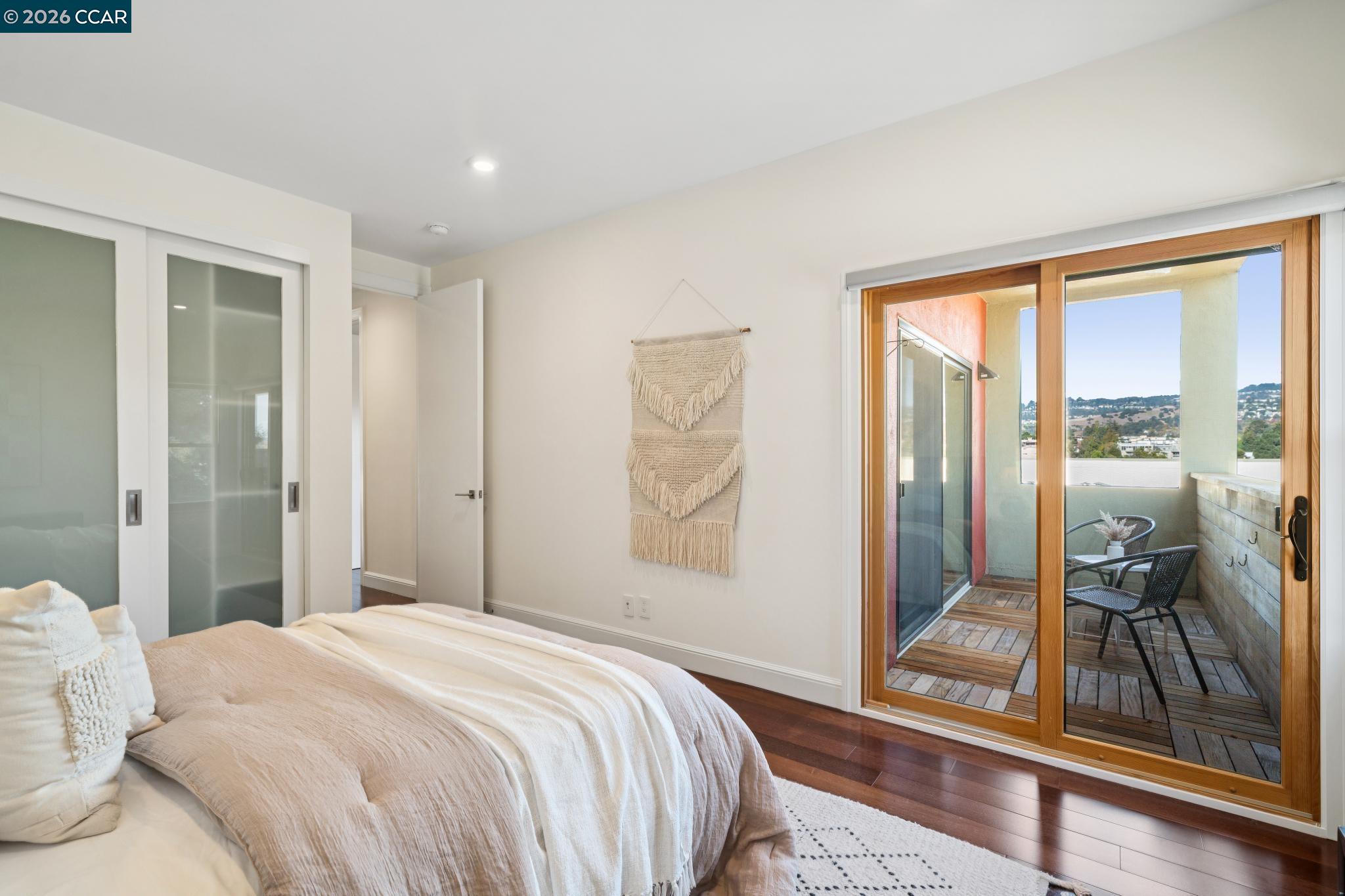 Staged bedroom with sliding glass doors opening to a furnished balcony and hillside views.