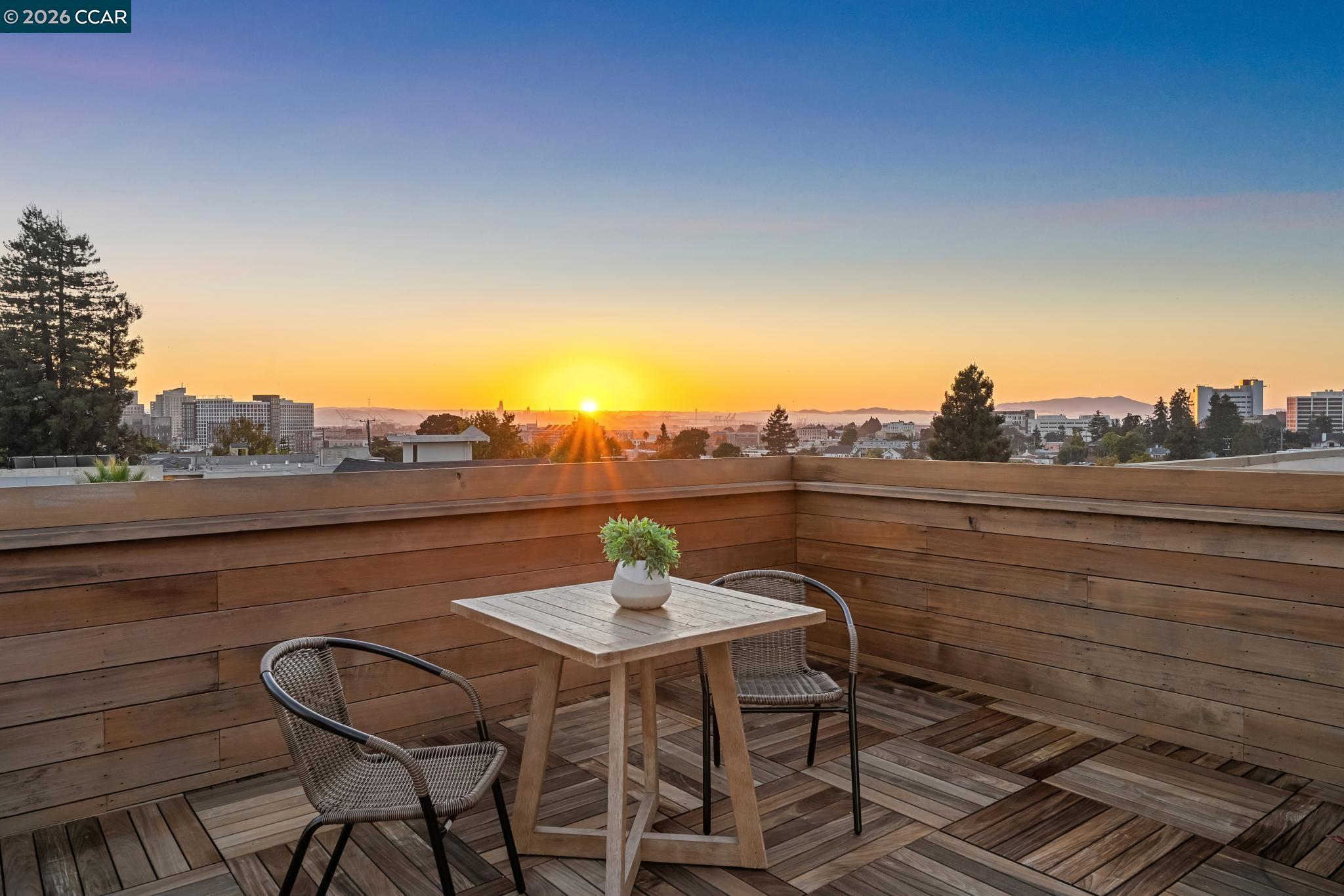 Rooftop deck with woven chairs and a table overlooking Oakland at sunset.