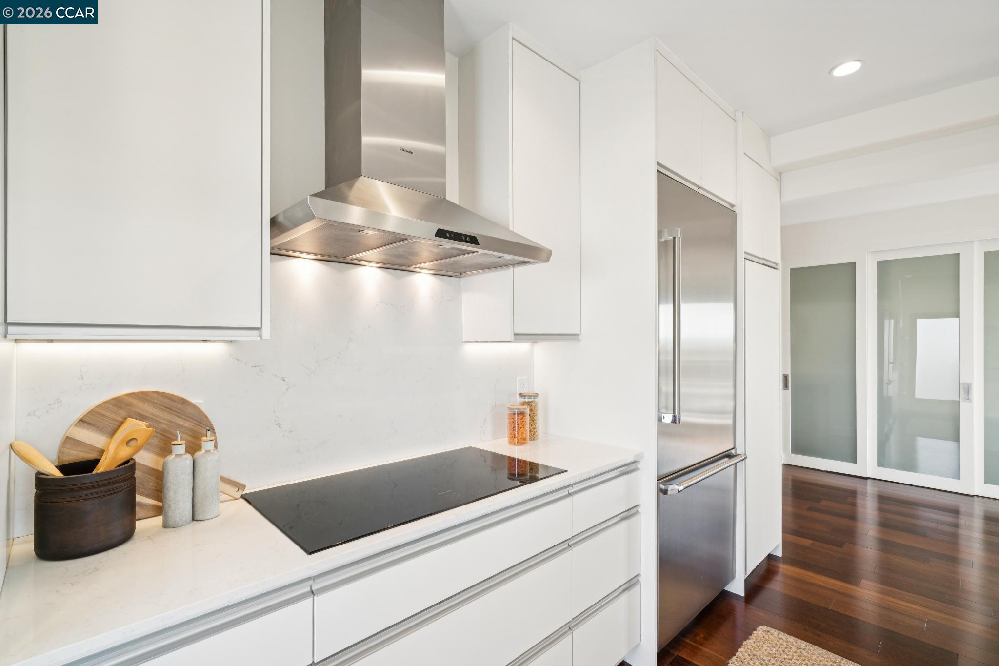 Modern white kitchen with a black induction cooktop, stainless-steel appliances, and dark hardwood floors.