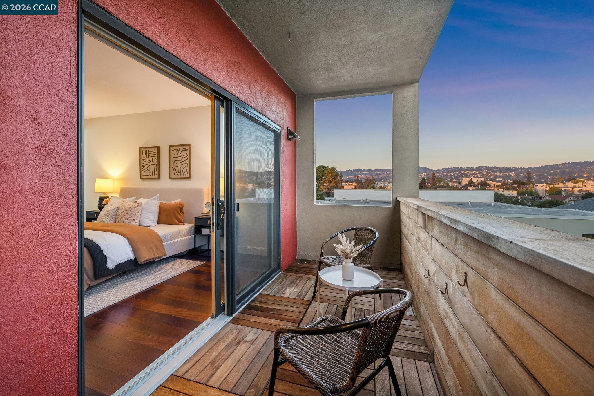 Apartment balcony with wood decking and woven seating overlooking Oakland hills, with an open view into the bedroom.