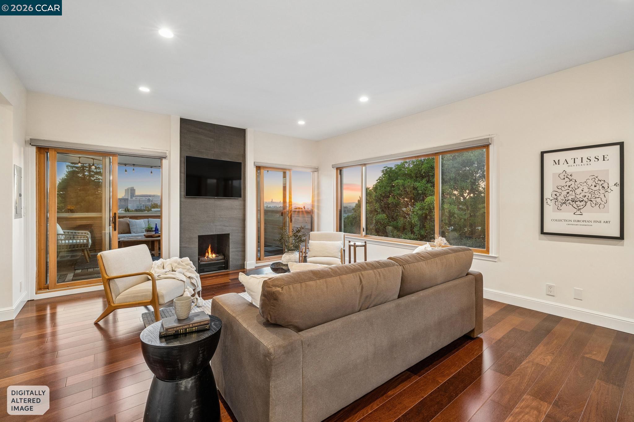 Living room with a brown sectional, fireplace, wood floors, and large windows glowing in sunset light.