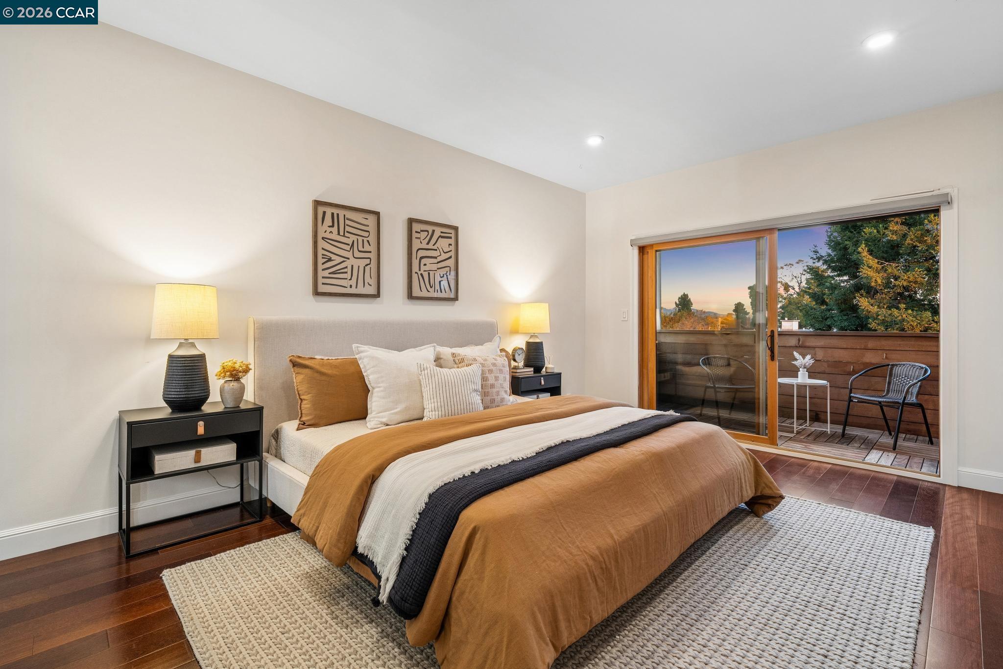 Staged bedroom with a king bed and sliding doors opening to a furnished balcony.