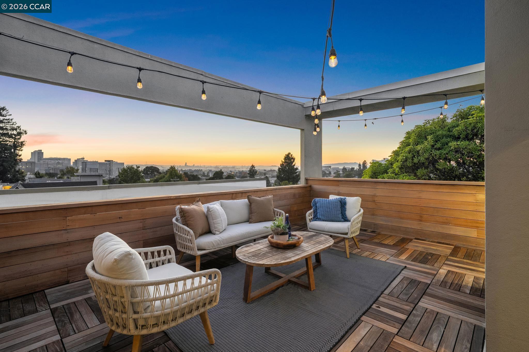 Rooftop deck seating overlooks Oakland at sunset beneath string lights.