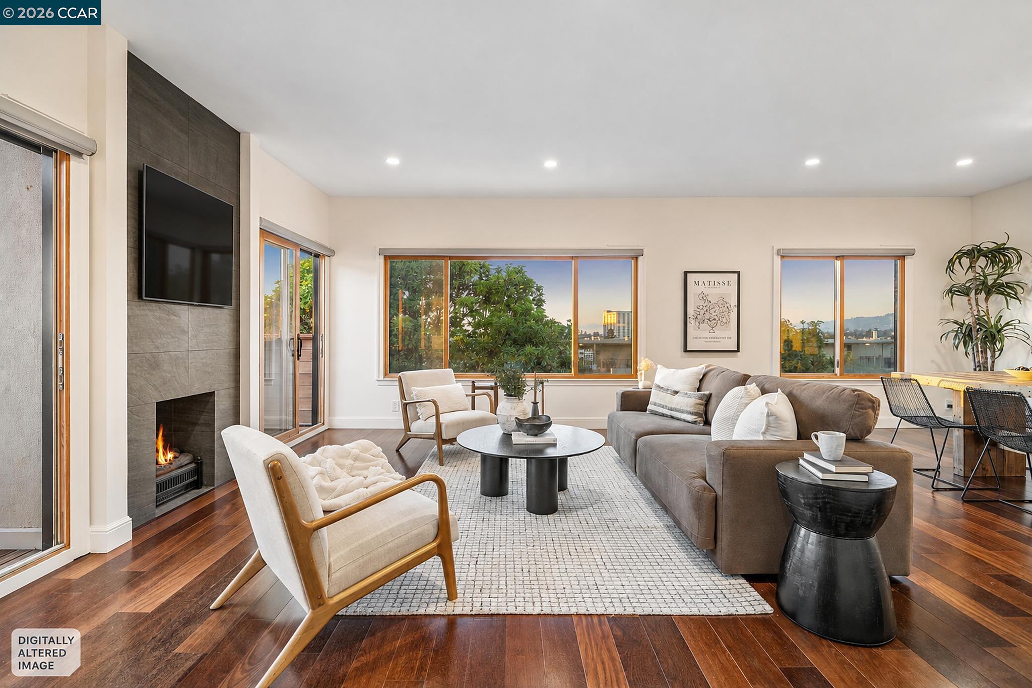 Staged living room with a fireplace, wide windows, gray sofa, and dark wood floors.