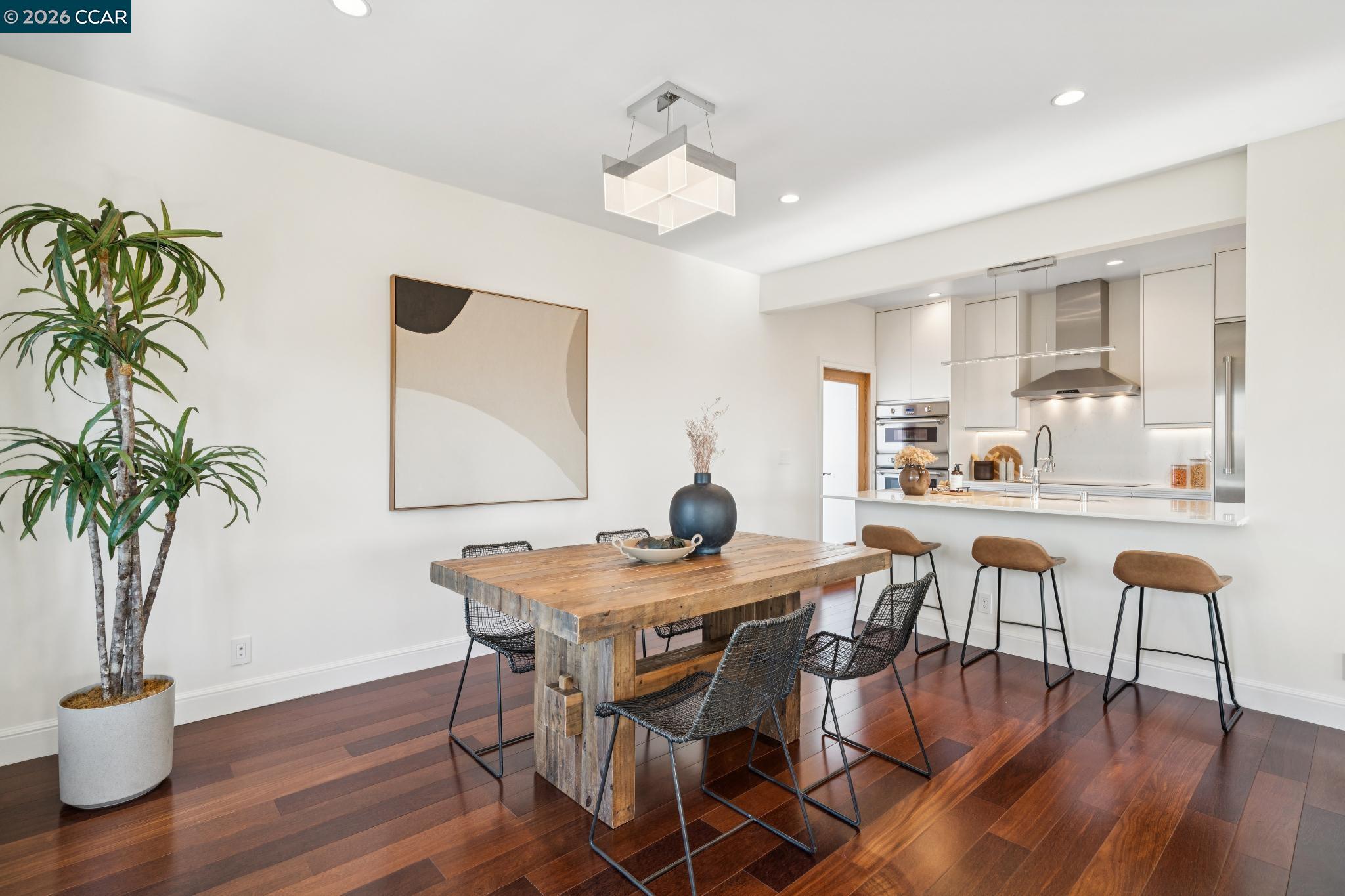 Open-plan dining area with a rustic wood table, dark hardwood floors, and a white kitchen with breakfast bar.