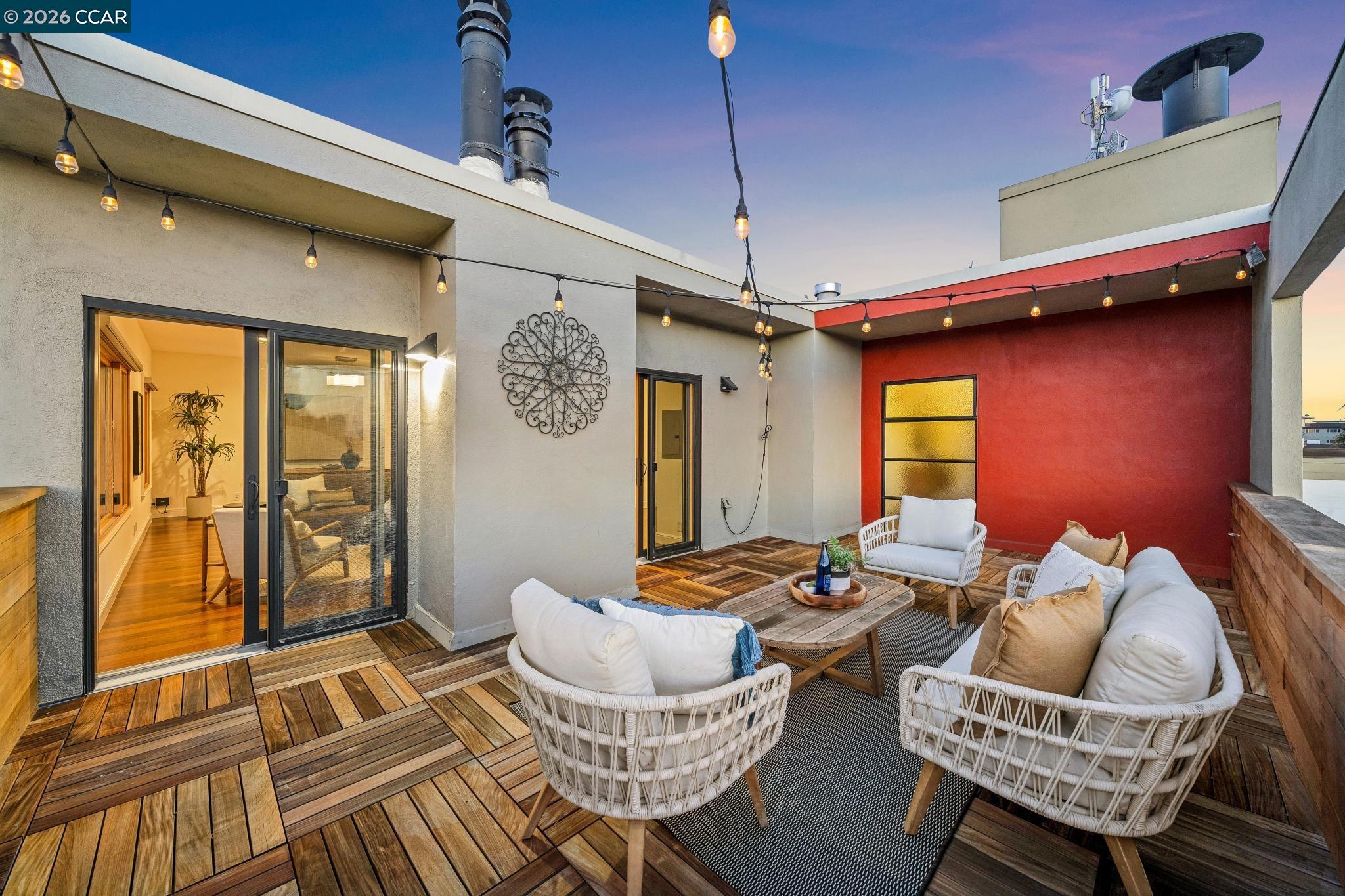 Rooftop terrace with white wicker seating, patterned wood decking, and string lights.