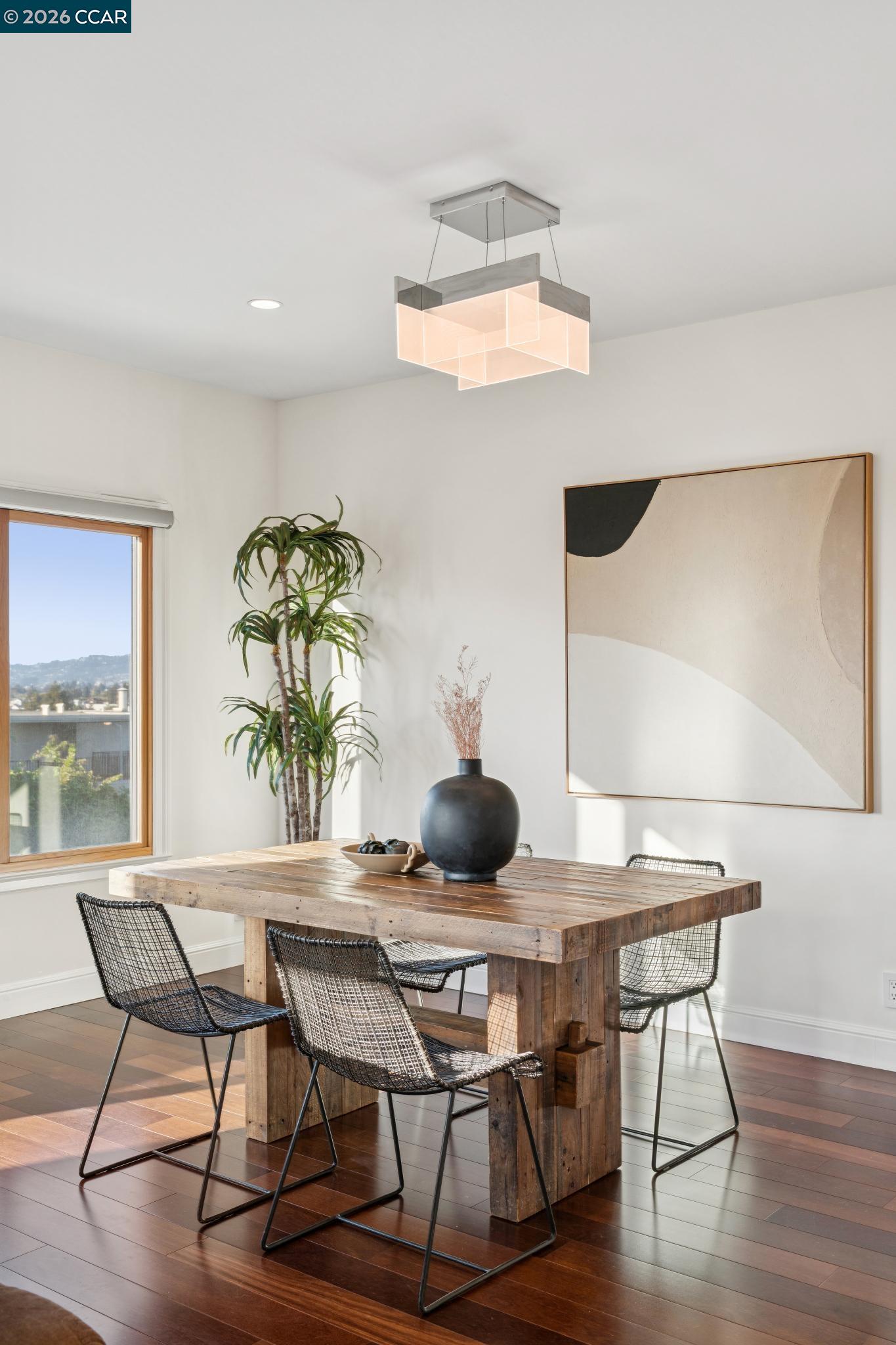Dining room with a rustic wood table, woven chairs, and a geometric pendant light.