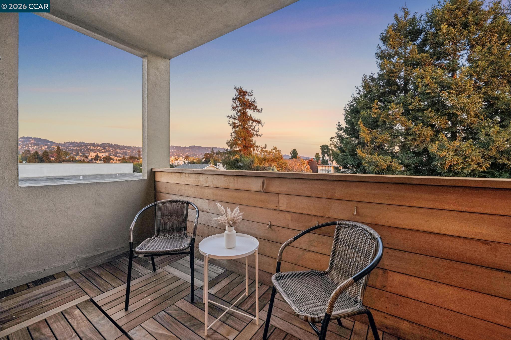 Furnished balcony with wicker chairs and sunset views over Oakland hills and buildings.