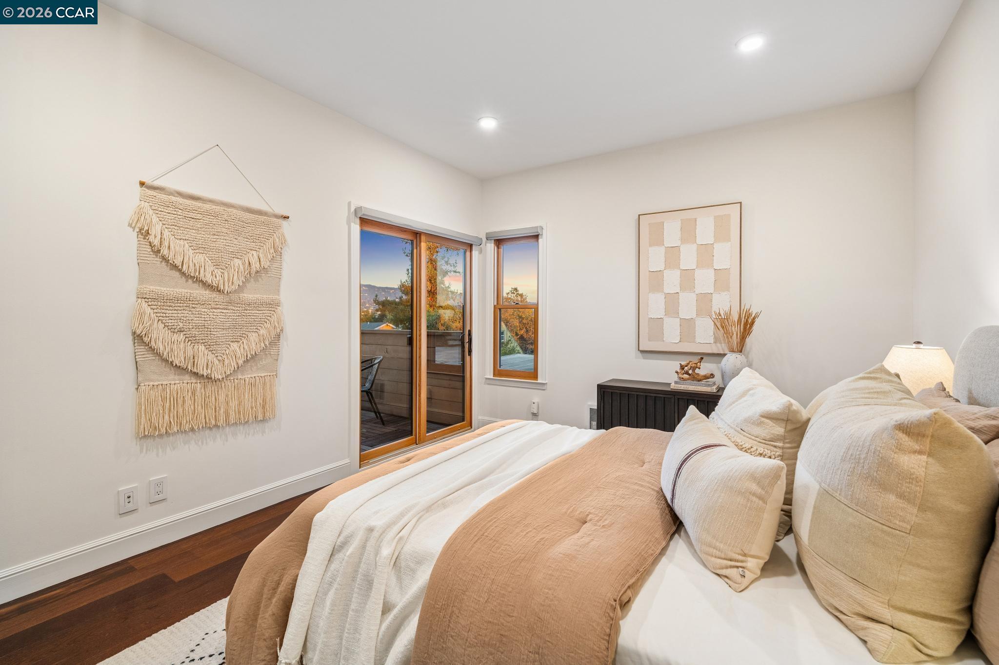Bedroom with a cream-and-tan bed, macramé wall hanging, and sliding doors to a deck.