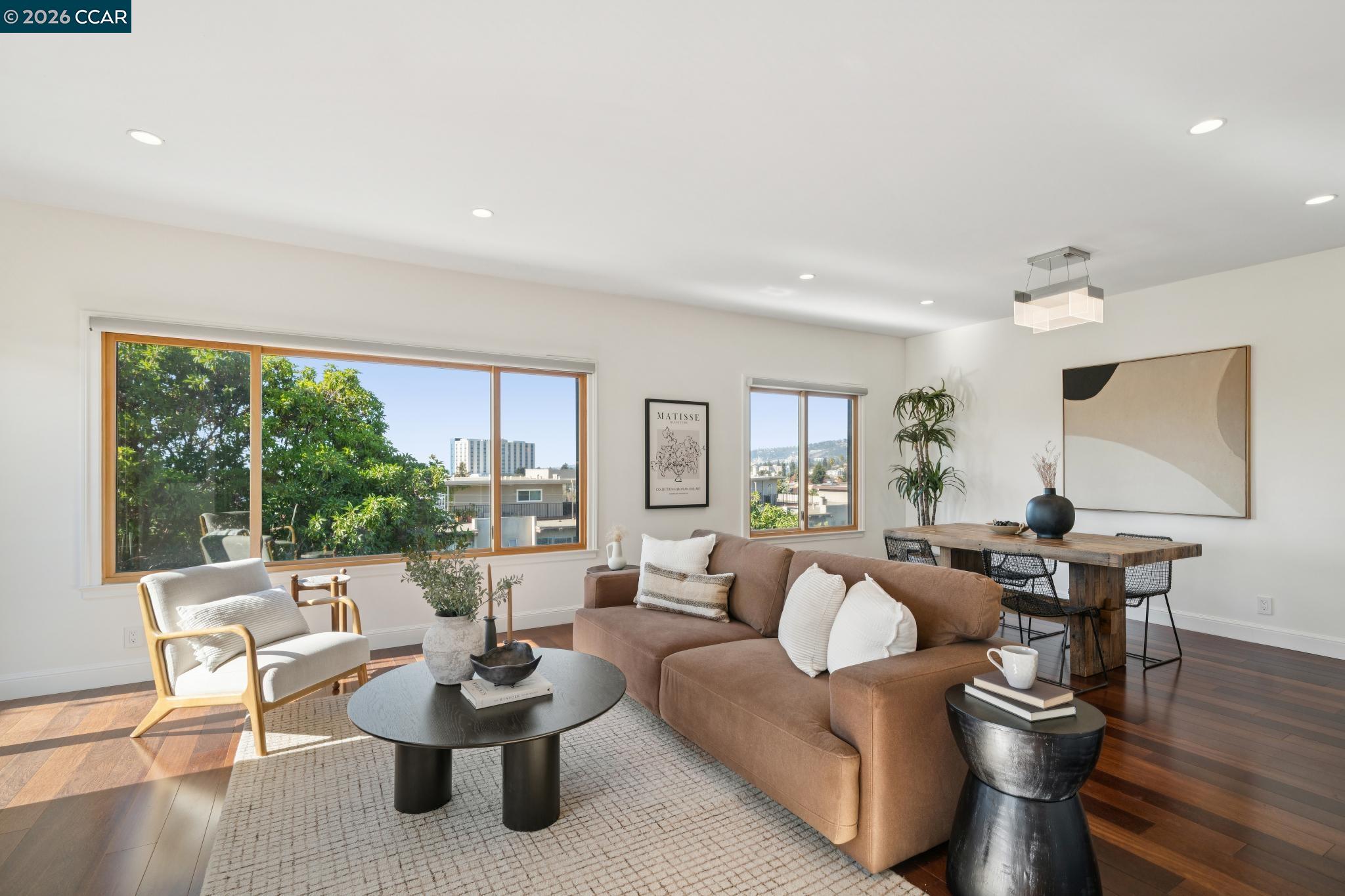 Staged living room with a brown sectional, large sunny windows, and an adjoining dining area.