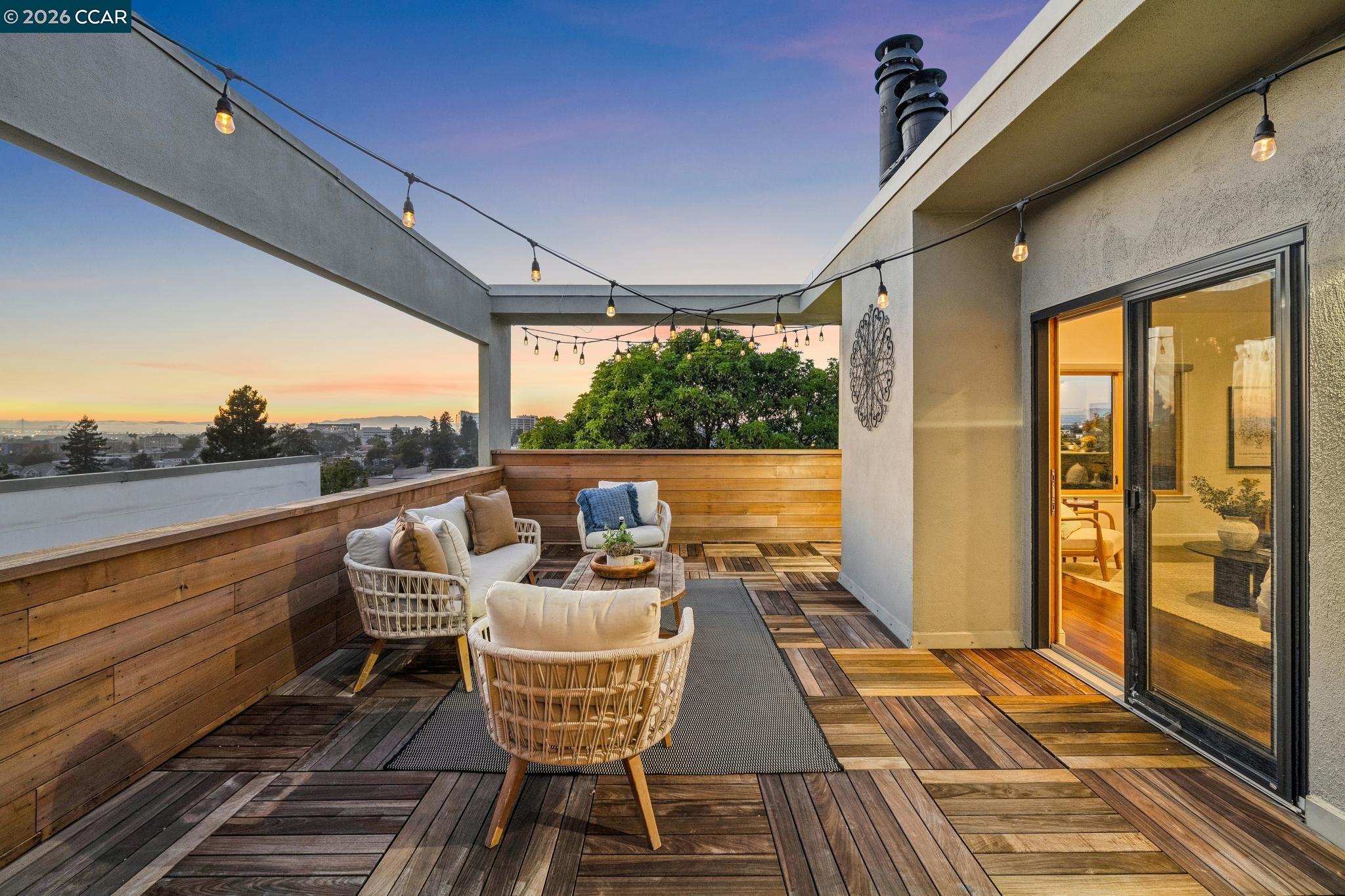 Furnished rooftop terrace with wood decking, string lights, and sunset city views.