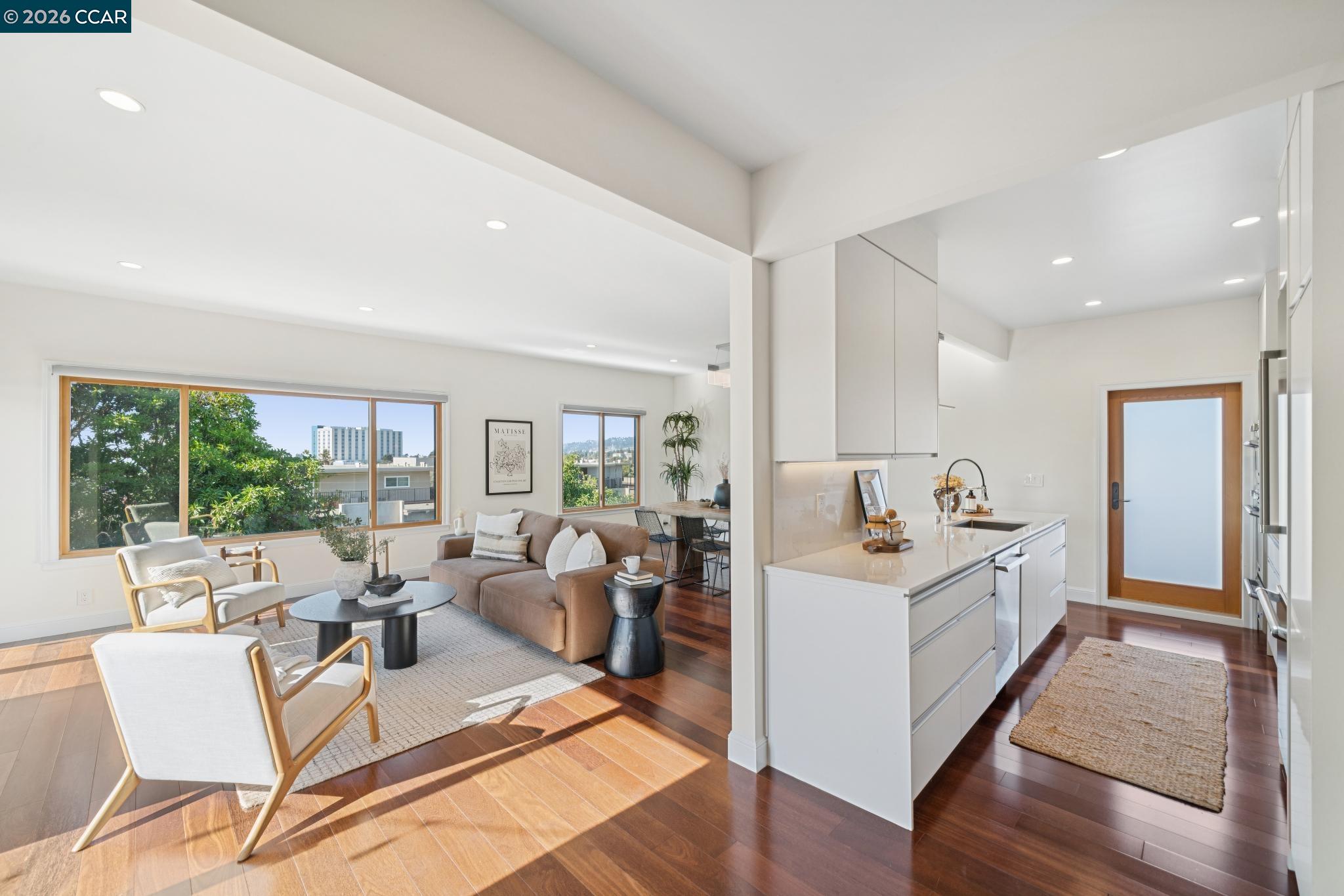 Open-plan condo living room and kitchen with a white island, hardwood floors, and large windows.
