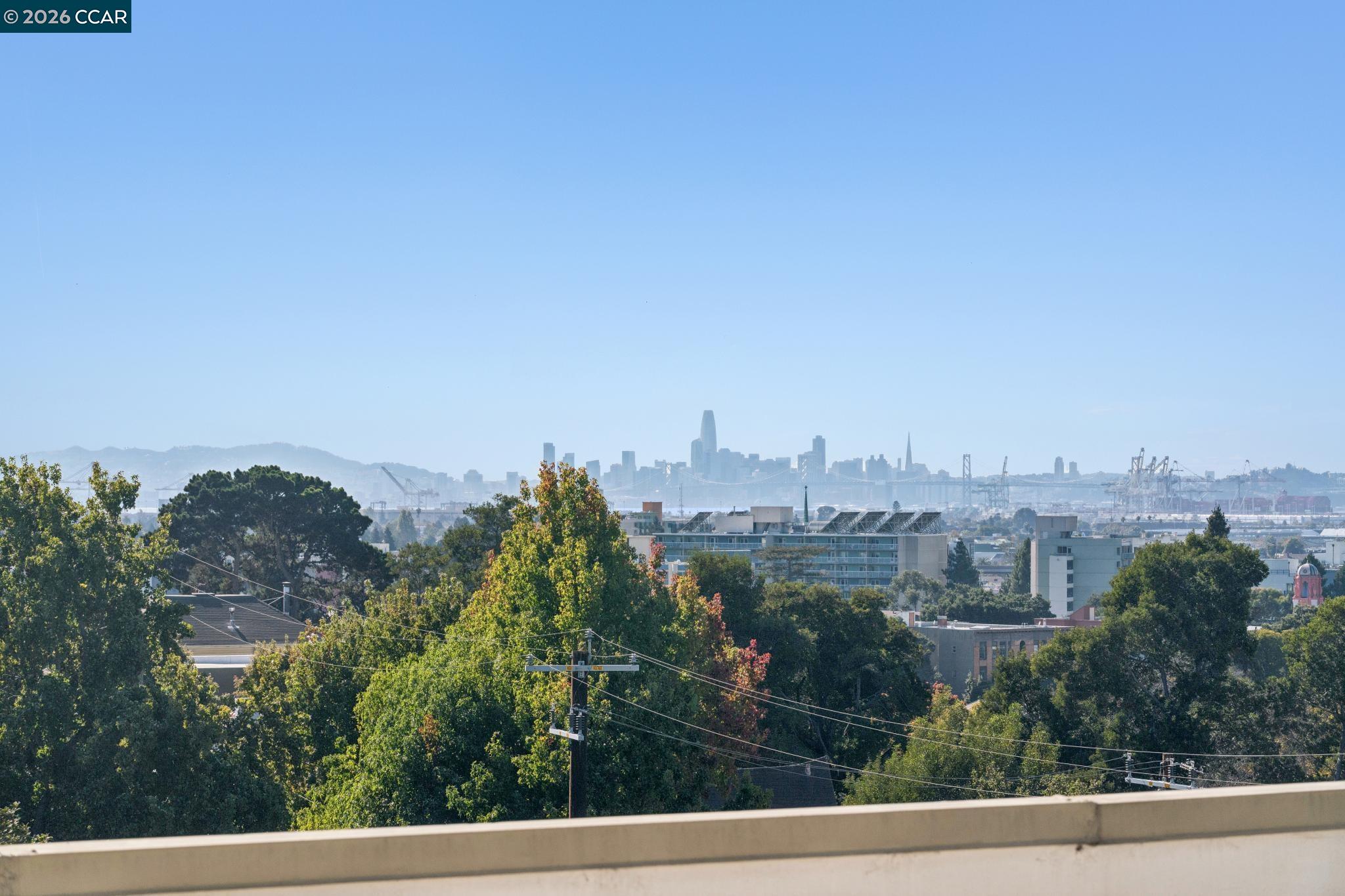 San Francisco skyline viewed from a balcony over Oakland rooftops and trees.