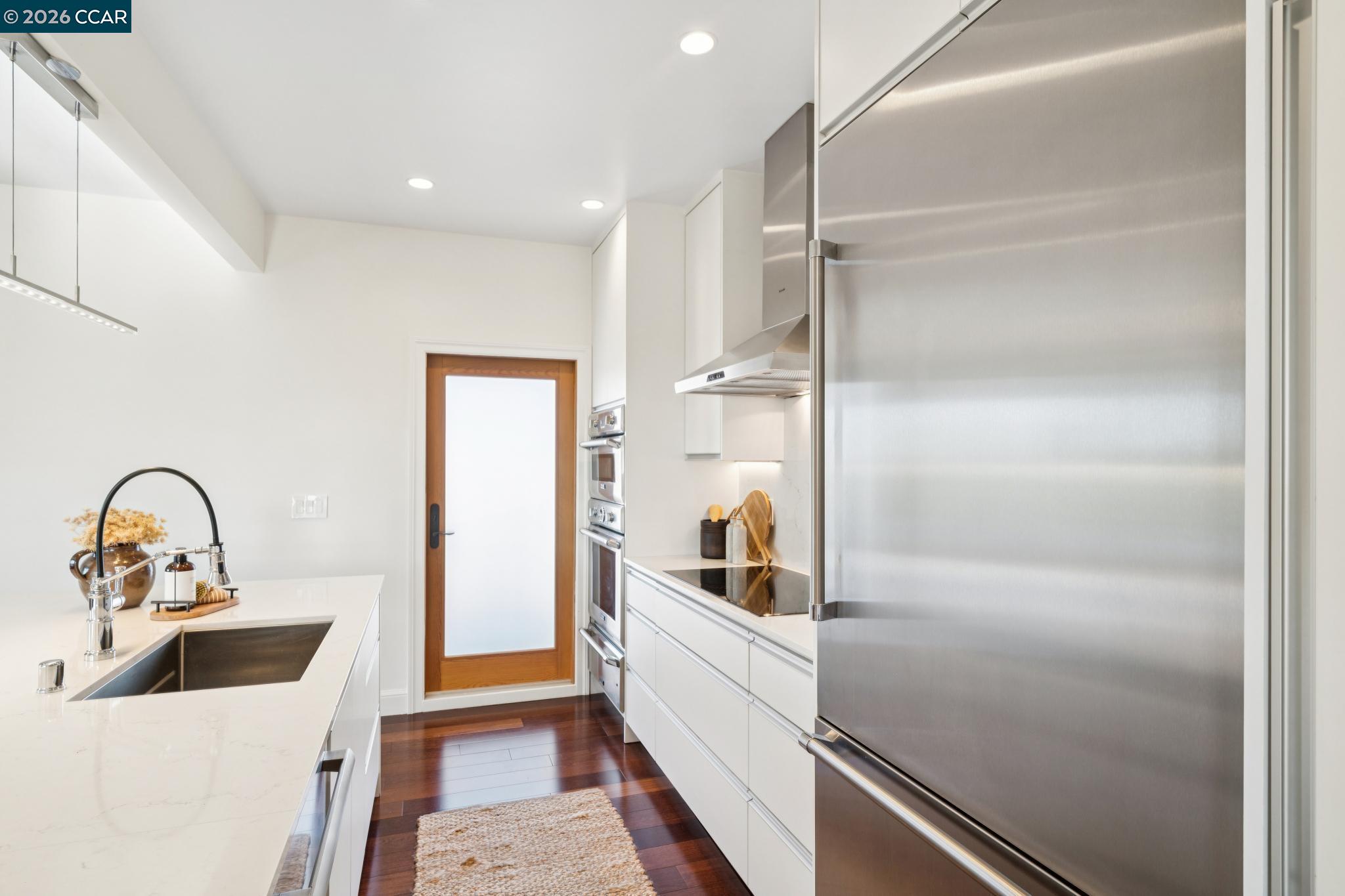 Modern kitchen with white cabinetry, stainless steel appliances, and a large island sink.